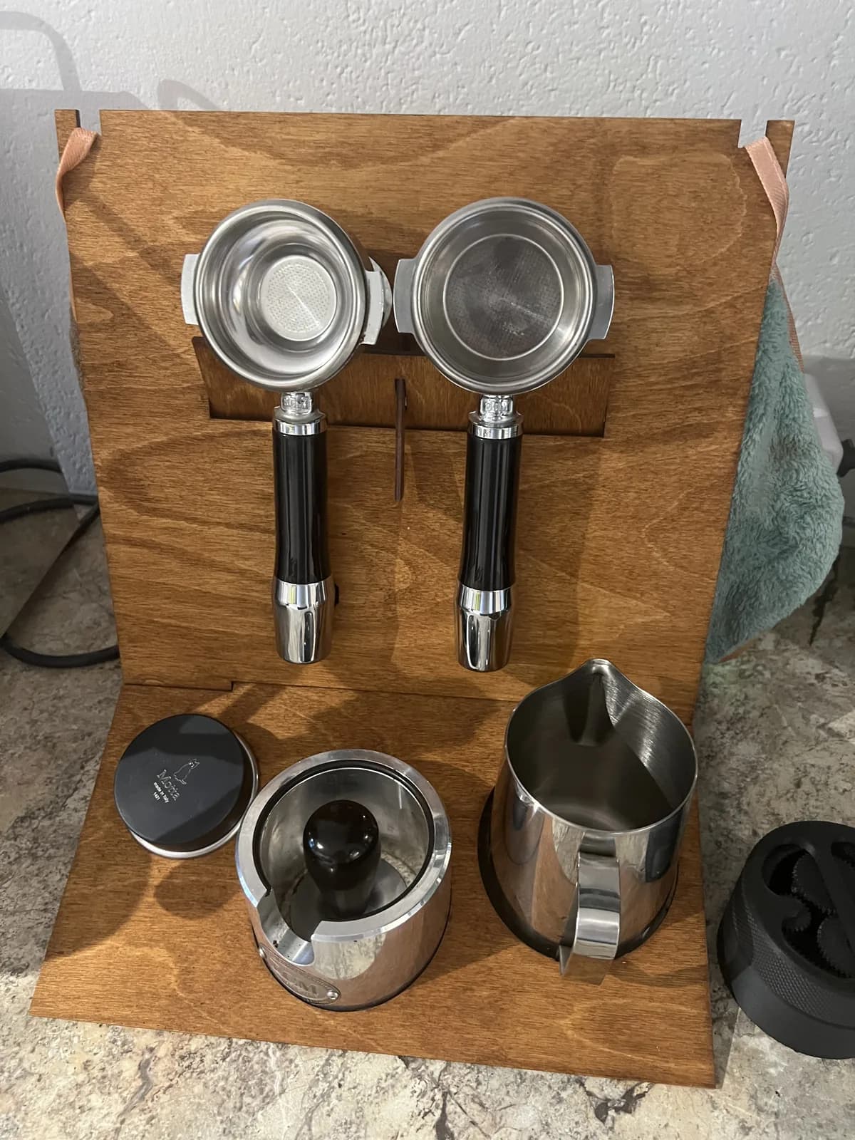 Estación barista vista desde arriba: dos portafiltros colgados y, debajo, un dosificador con tapa y una jarra de leche en las aberturas redondas de la bandeja