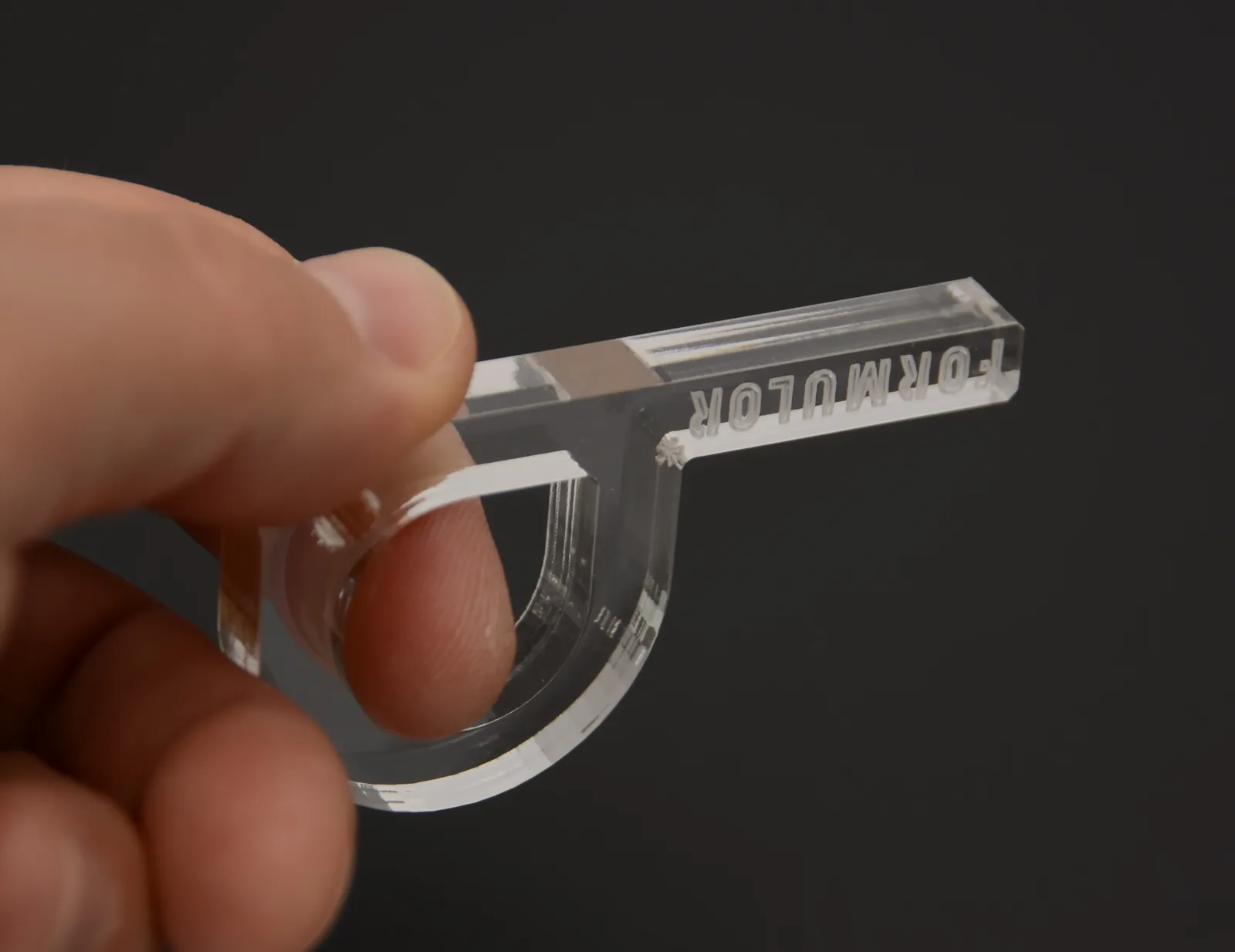 Eine Hand hält den Anhänger vor dunklem Hintergrund — die Finger sind durch das klare Acryl zu sehen