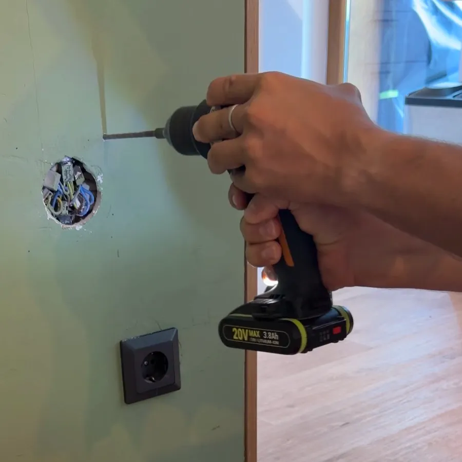 Ein Akkubohrer setzt neben der offenen Dose ein Loch in die Wand