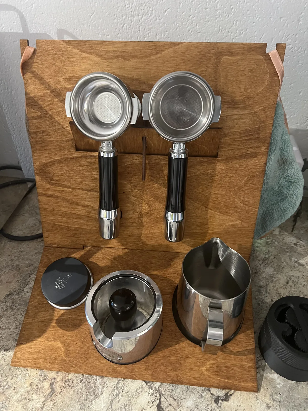 Estación barista vista desde arriba: dos portafiltros colgados y, debajo, un dosificador con tapa y una jarra de leche en las aberturas redondas de la bandeja