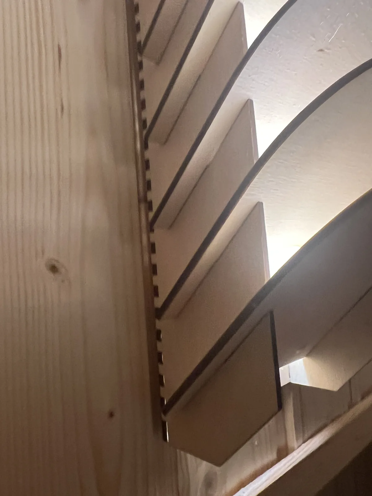 Blick von der Seite auf das Rückgrat der Leuchte: eine senkrechte Sperrholzplatte mit dicht gereihten Kammschlitzen, in denen die Lamellen stecken